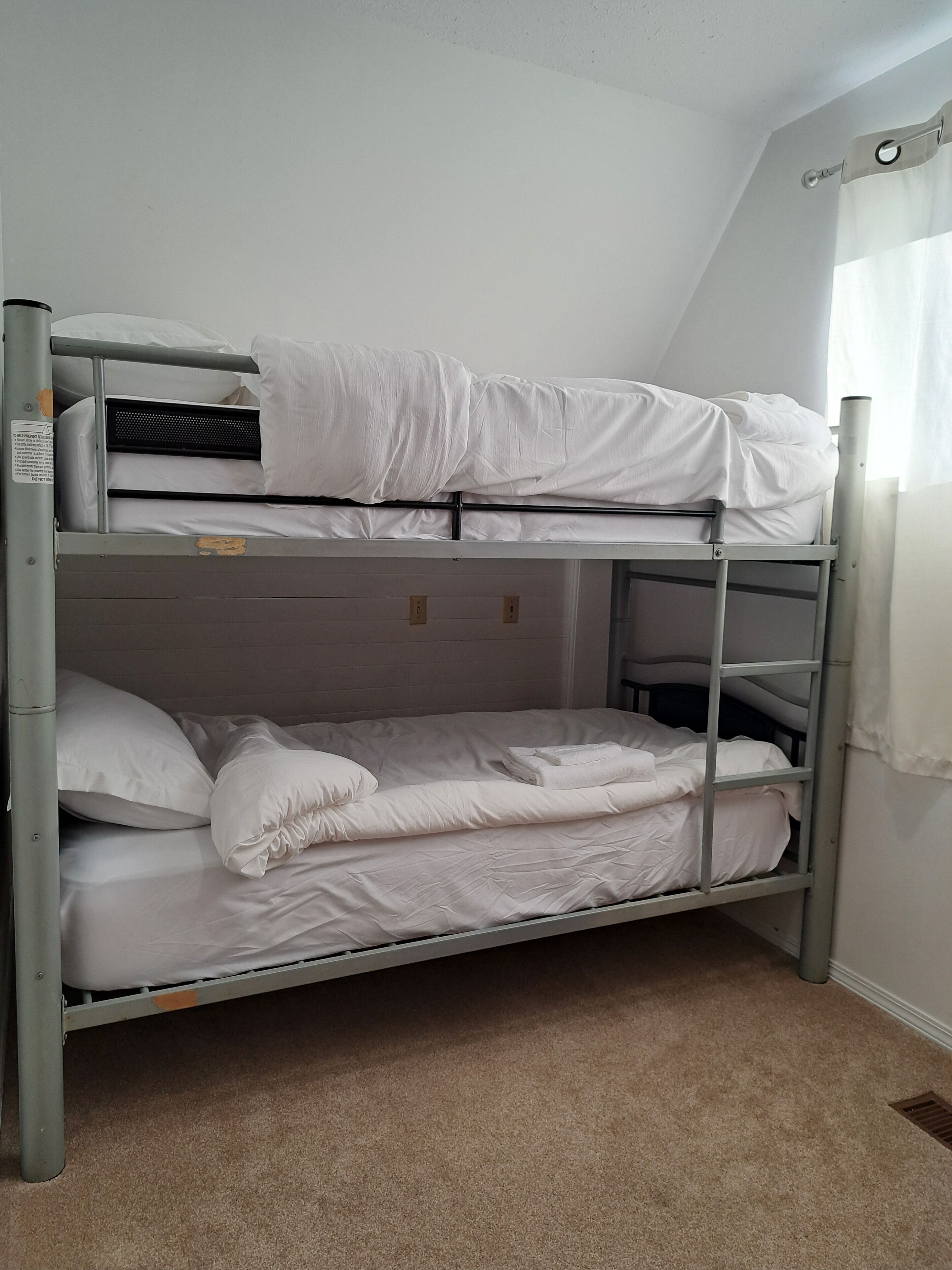 A bunk bed with white bedding in a room with beige carpet and white walls.