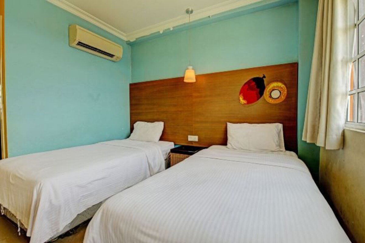 A room with two single beds, a wooden headboard, an air conditioning unit, and a window with curtains.