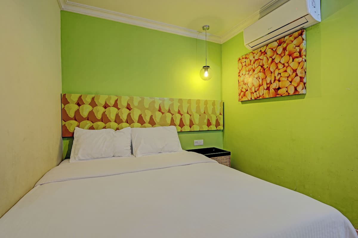 A room with a bed, green walls, a patterned headboard, a wall-mounted air conditioner, and a wall art piece.