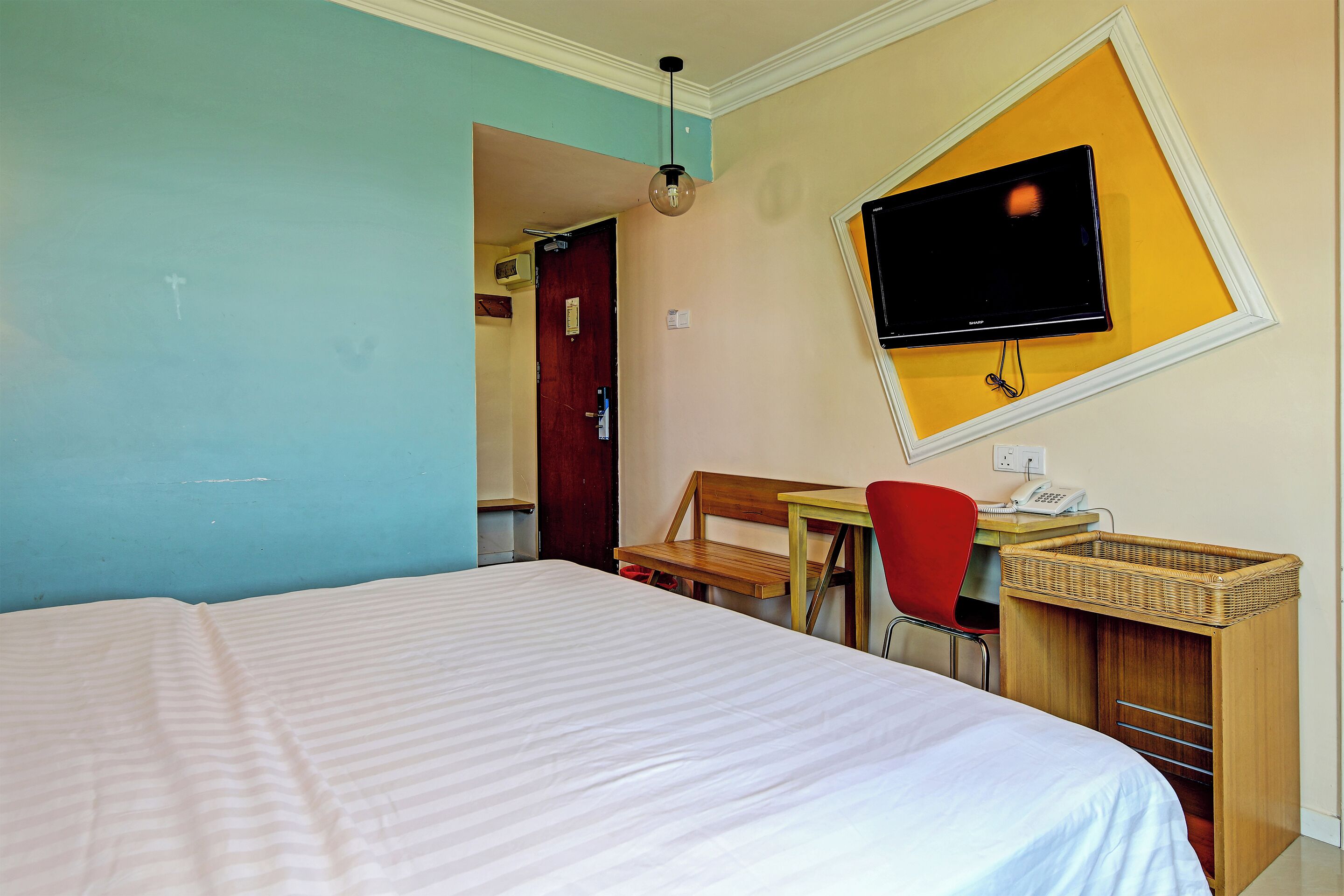 A hotel room with a bed, a desk with a chair, a television mounted on the wall, and a small table with a telephone.