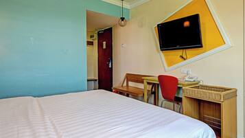 A hotel room with a bed, a desk with a chair, a television mounted on the wall, and a small table with a telephone.