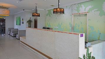 Un área de recepción con mostrador de mármol, dos candelabros, mostrador de recepción y una pared verde con un mapa.