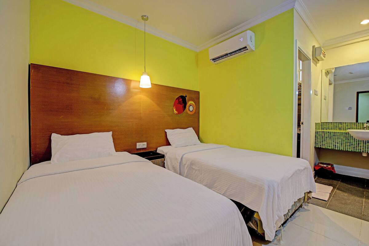 A hotel room with two beds, a wooden headboard, a wall-mounted air conditioner, and a bathroom with a green checkered sink.