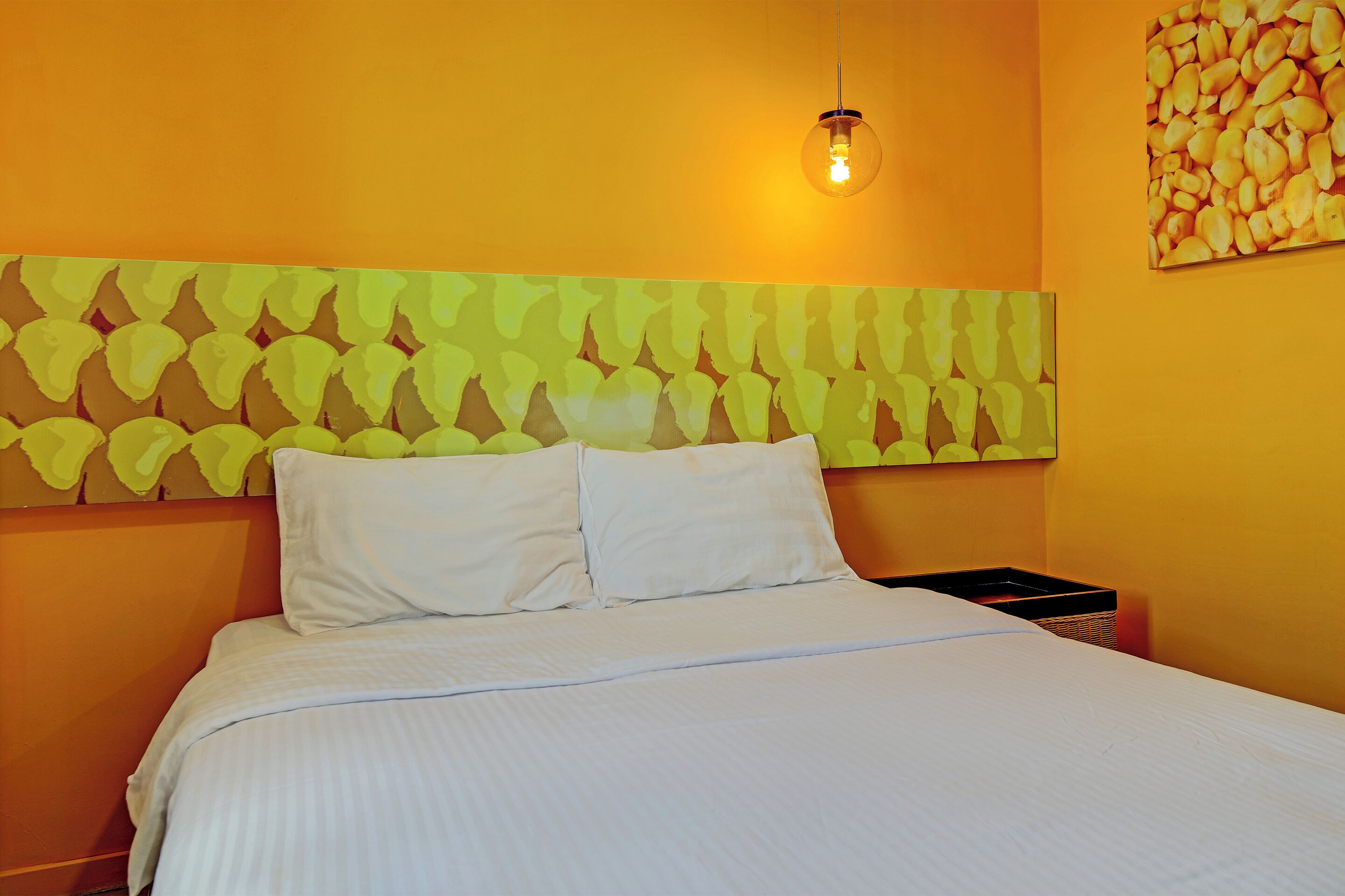 A neatly made bed with white linens, a headboard with a leaf pattern, and a single light bulb hanging above.