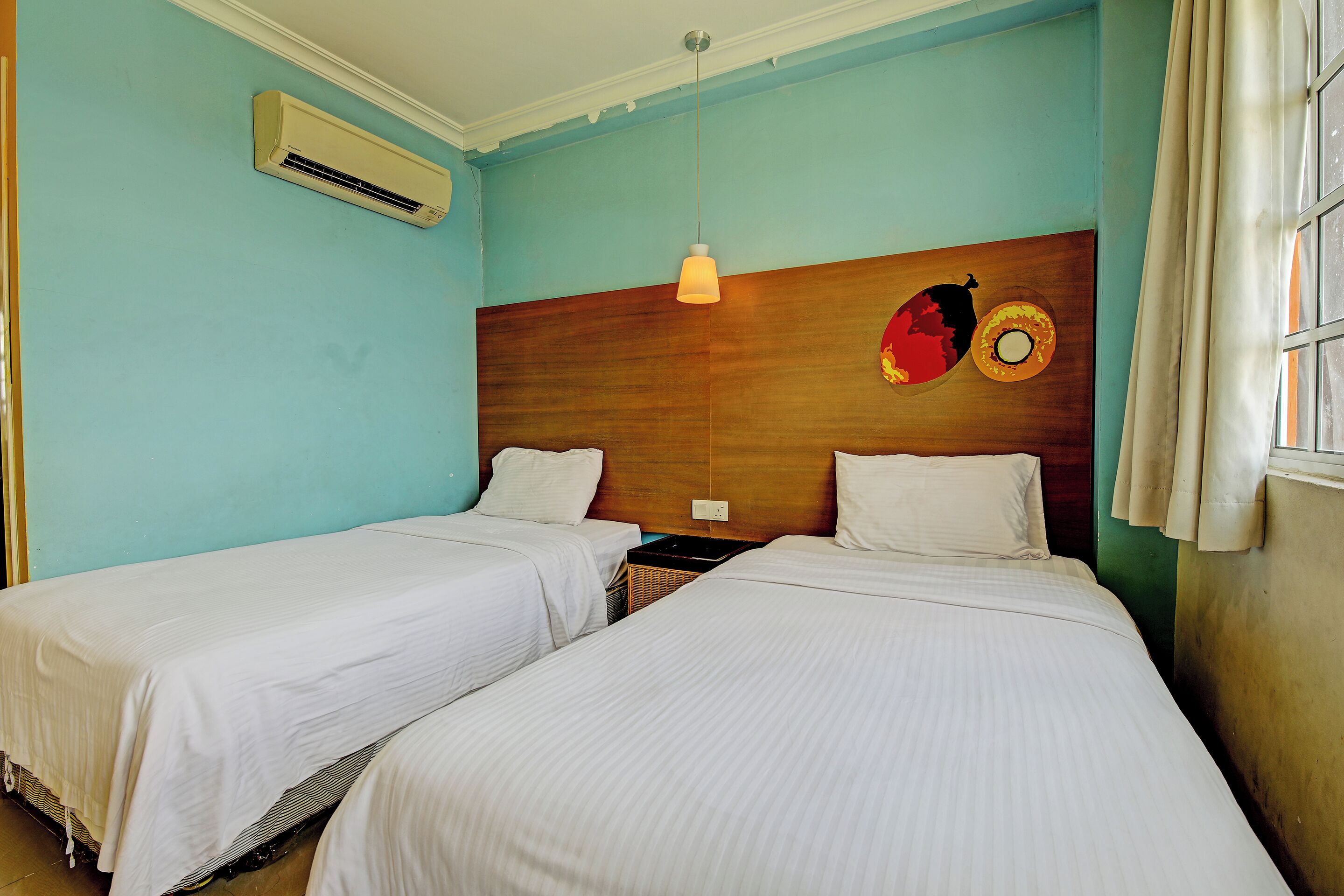 A room with two beds, an air conditioning unit, a hanging light fixture, and a wall decoration.