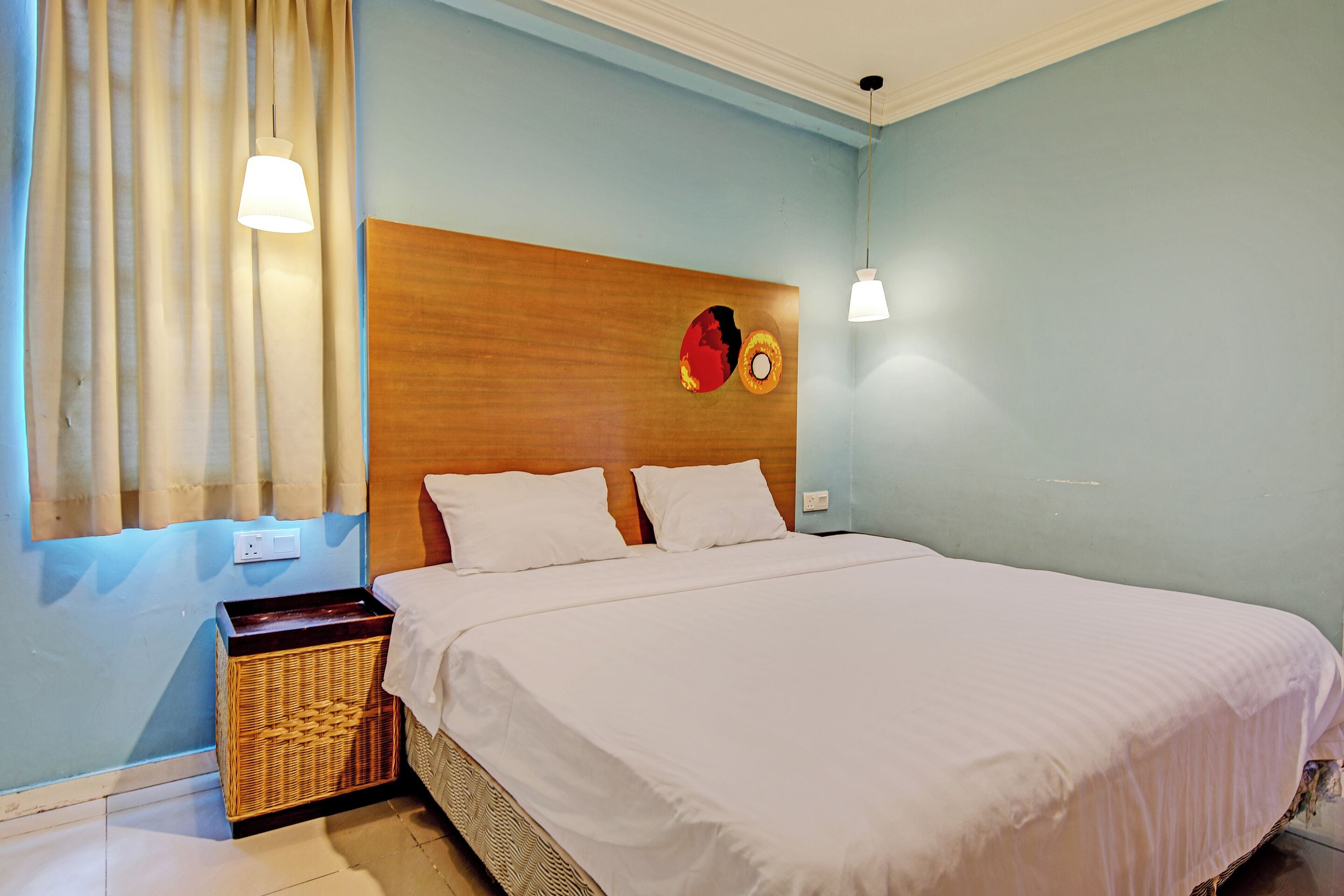A neatly made bed with white linens, a wooden headboard, and a wall-mounted clock.