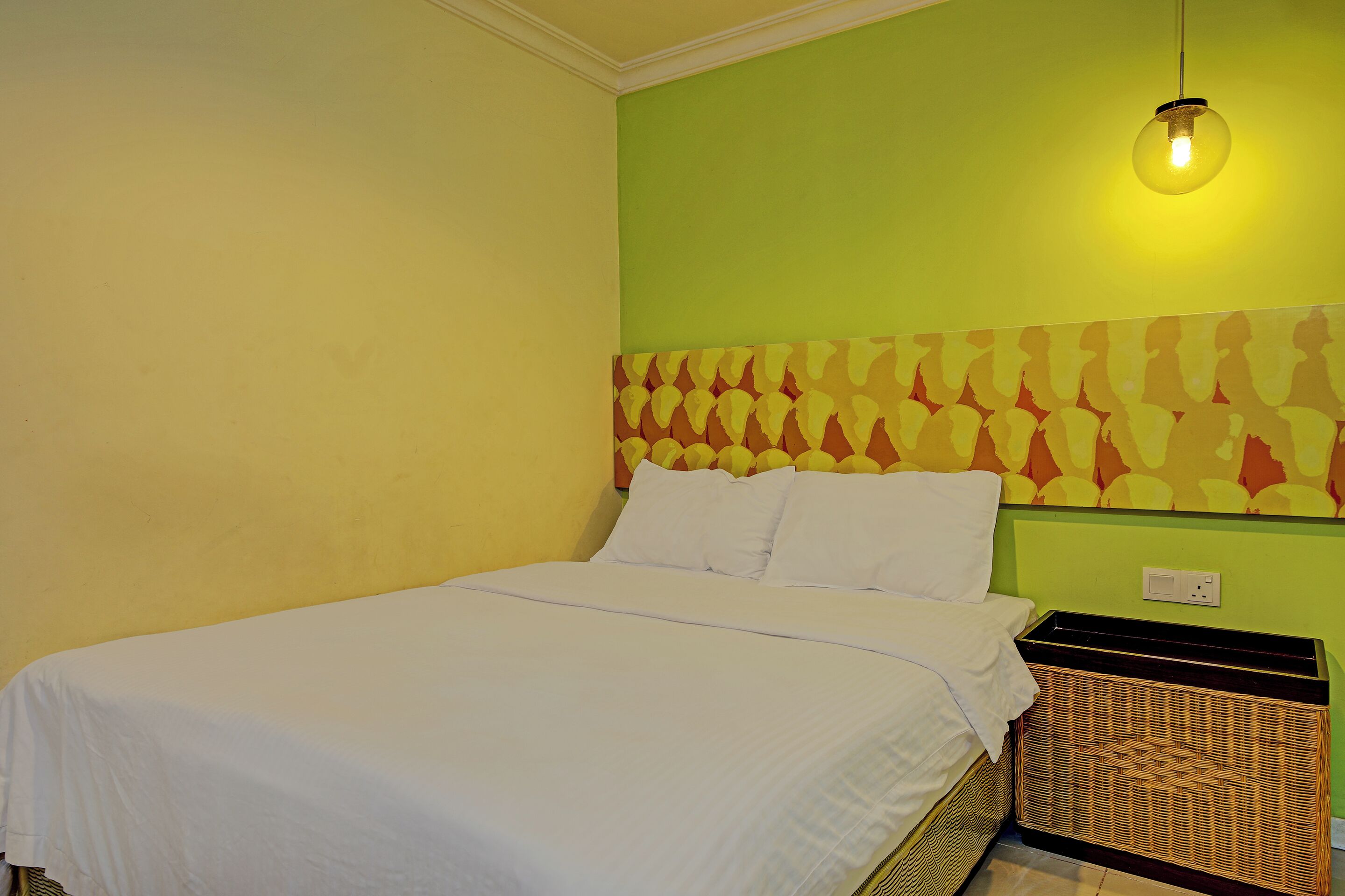 A neatly made bed with white linens in a room with green walls and a patterned headboard.