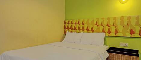 A neatly made bed with white linens in a room with green walls and a patterned headboard.