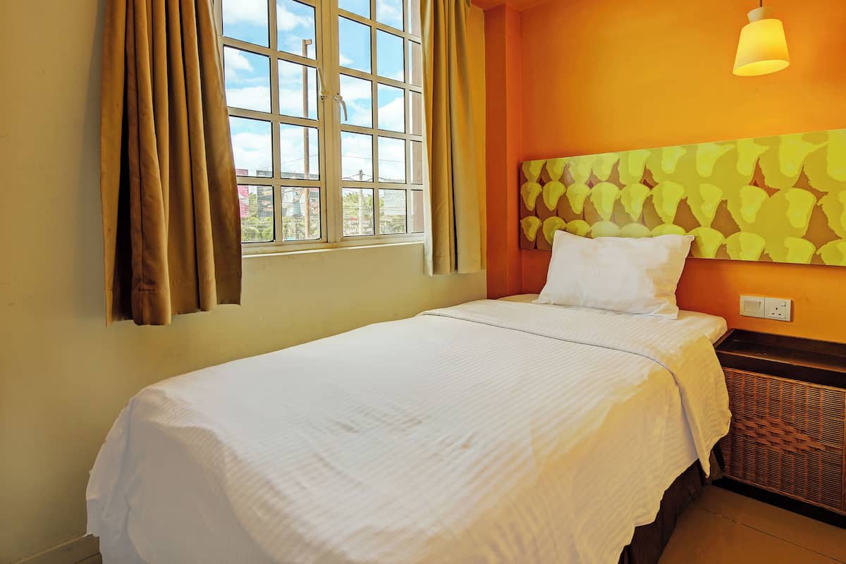 A hotel room with a bed, a window with curtains, a wall-mounted light fixture, and a patterned wall design.