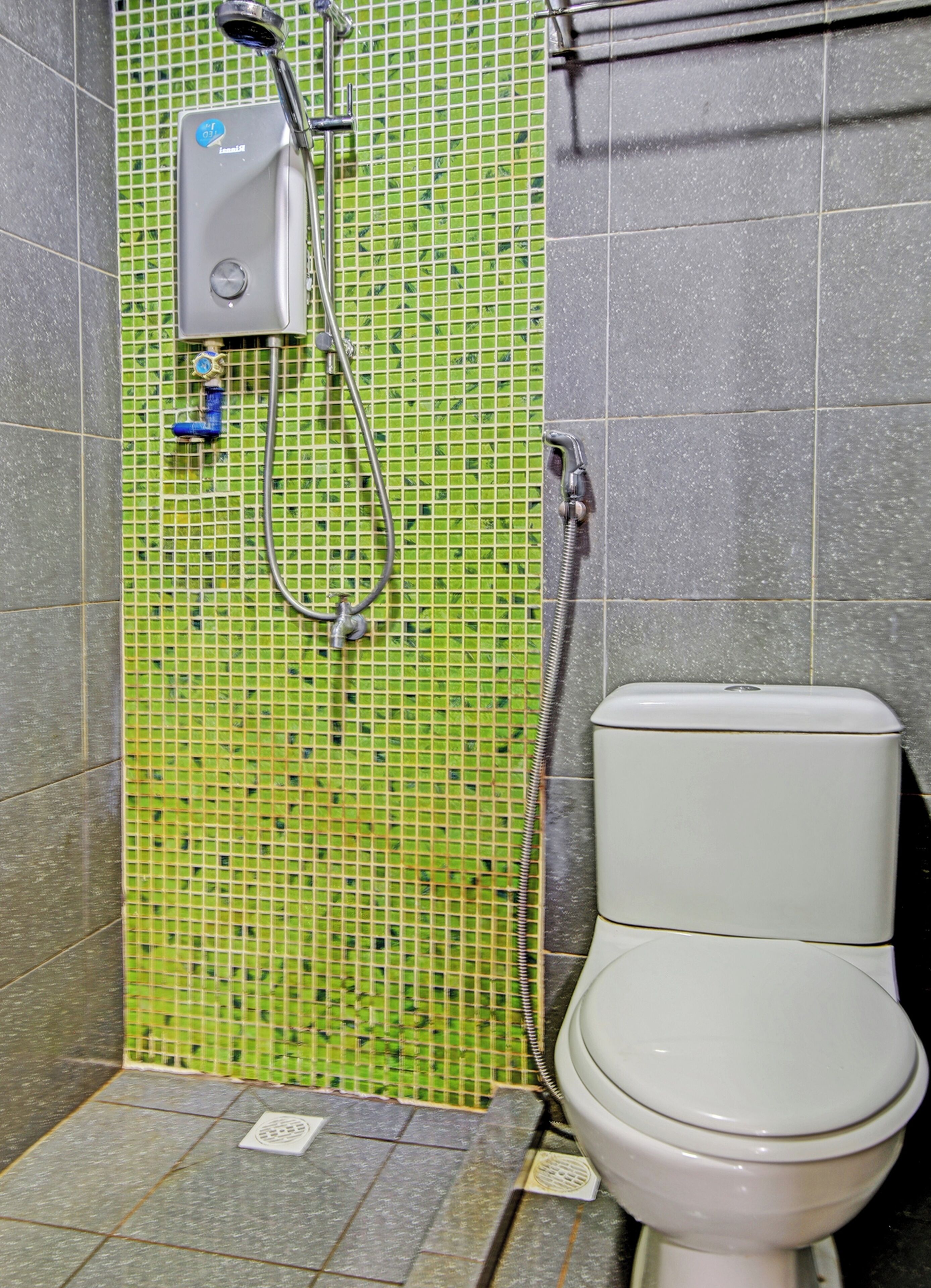 A bathroom with a green mosaic wall, a white toilet, and a shower unit.