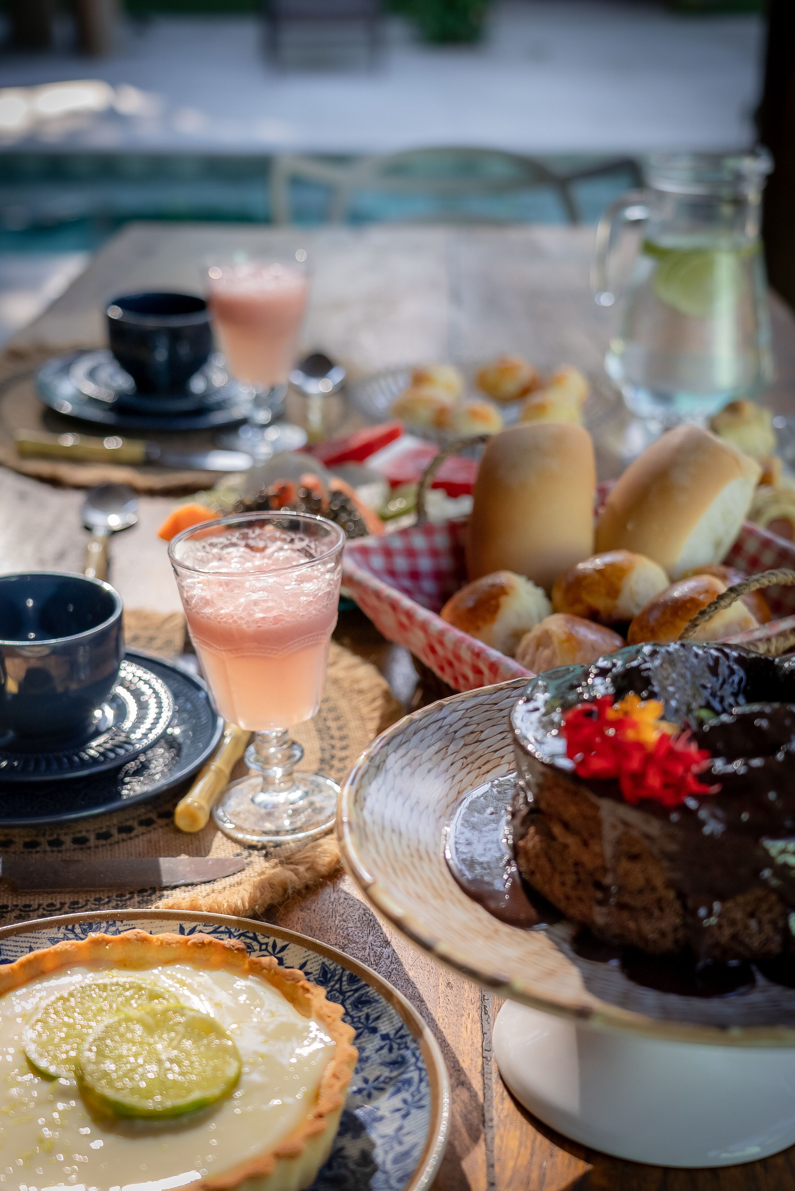 Una mesa con diversos alimentos, incluyendo un pastel de chocolate, panes y un vaso de bebida rosada.