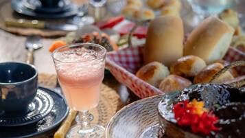 Una mesa con diversos alimentos, incluyendo un pastel de chocolate, panes y un vaso de bebida rosada.