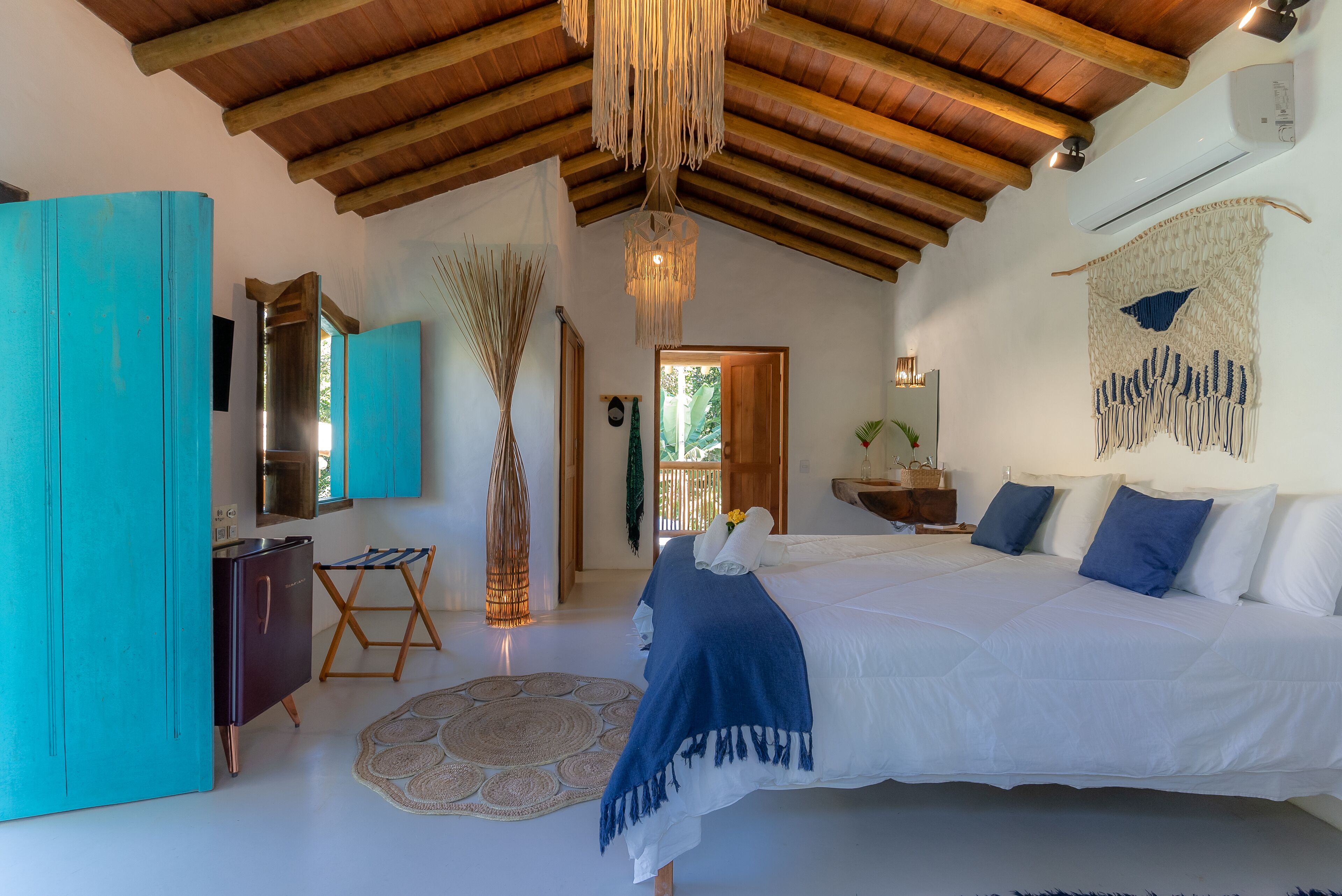 A bedroom with a large bed, wooden ceiling beams, a hanging light fixture, and a wall-mounted air conditioner.