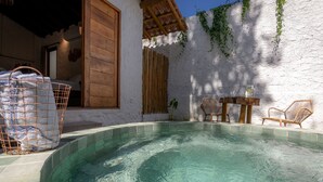Zona de piscina con superficie de agua cristalina, rodeada por un muro blanco con contraventanas de madera y una cerca de bambú. Hay sillas de mimbre y una pequeña mesa con bebidas.