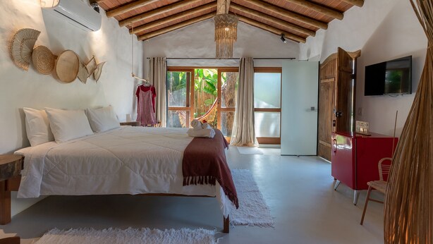 Un dormitorio con una cama, un aparador rojo, una televisión y un ventanal con vistas a zonas verdes.