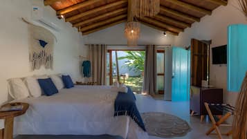 Une chambre spacieuse avec un grand lit, des poutres apparentes en bois au plafond, un luminaire suspendu et une vue sur l’extérieur.