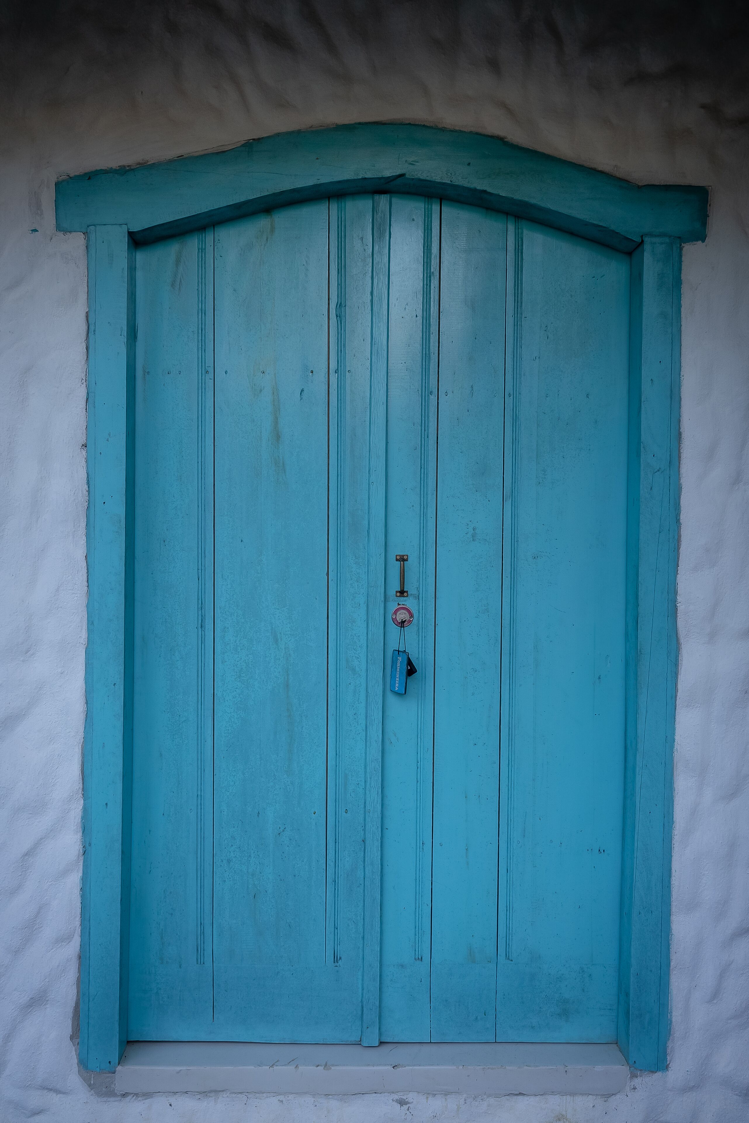 Una puerta turquesa con un picaporte sencillo y un pequeño candado.