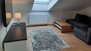 Quarto moderno no estilo loft com claraboia, sofá, mesa de centro e escrivaninha com luminárias.