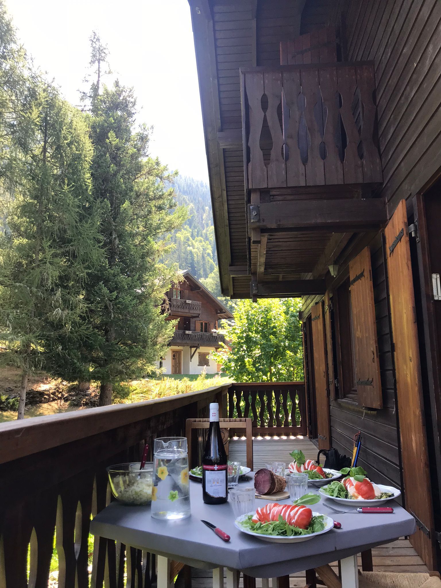 Une terrasse en bois avec une table dressée pour un repas, donnant sur une zone boisée.
