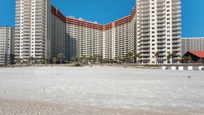 Ett stort hotell med flera våningar och balkonger, en sandstrand i förgrunden och palmer.