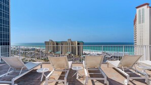 Ein Balkon mit Liegestühlen und Tischen mit Blick auf Strand und Meer.