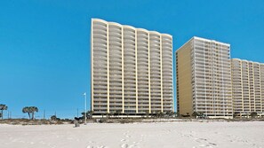 Un hotel sulla spiaggia con numerosi balconi e una spiaggia sabbiosa in primo piano.