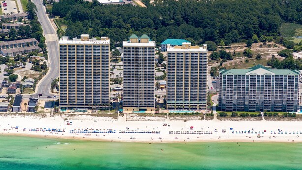 A beachfront hotel with multiple high-rise buildings, a beach in the foreground, and a road curving through the area. - Gulf-Front, Sweeping Views, 2 Pools, Sleeps 6 + Free Attraction Tickets! (Panama City Beach)