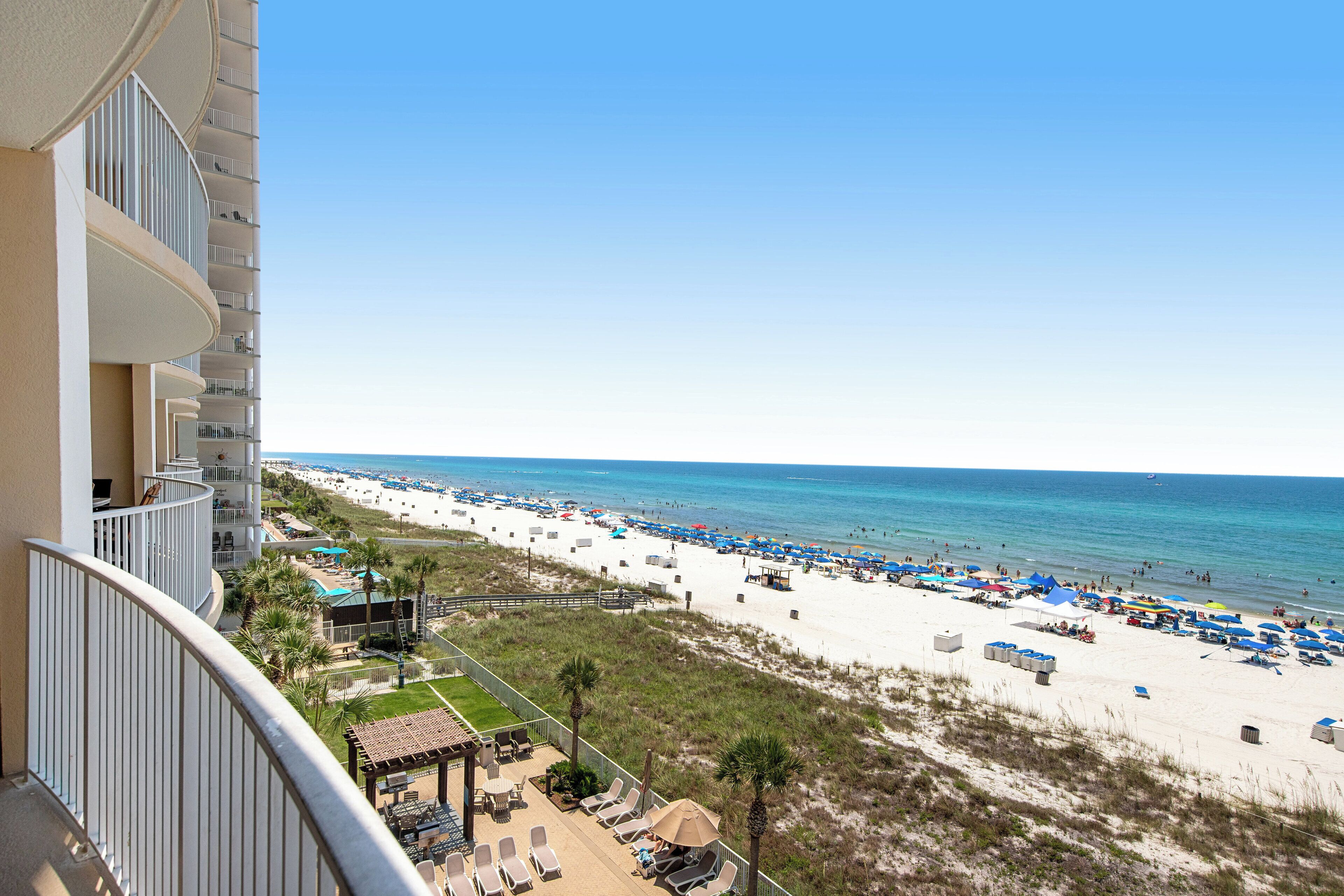 A beachfront hotel with balconies, a pool, and beach umbrellas.