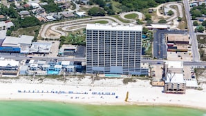 Eine Vogelperspektive eines Hotels mit großem Parkplatz, einem Schwimmbad und einem Strandbereich mit Sonnenschirmen.