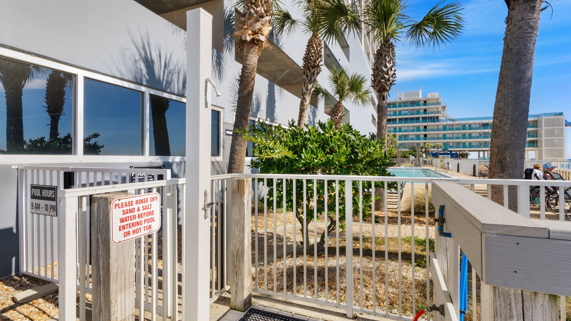 A pool area with a sign instructing to rinse off sand and salt water before entering the pool.