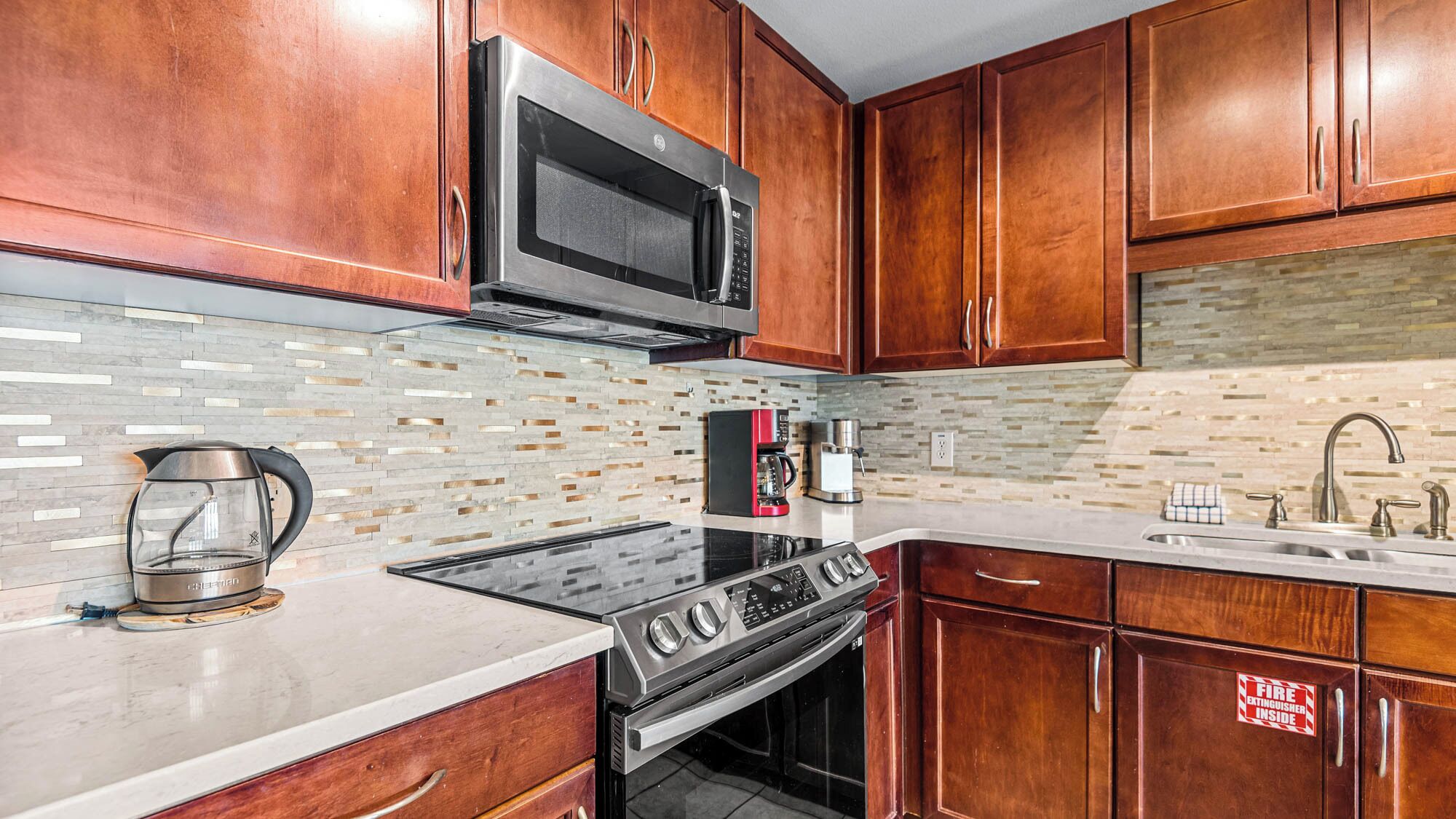 A modern kitchen with wooden cabinets, a stainless steel microwave, a coffee maker, and a stove.