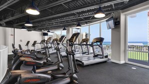 Ein Fitnessraum mit mehreren Cardiogeräten, großen Fenstern und Meerblick.