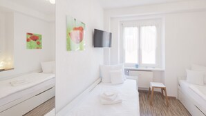 Hotellihuone, jossa on sänky, pieni pöytä, televisio ja taideteoksia seinällä.