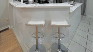 Una cocina moderna con armarios blancos, una isla central con taburetes y electrodomésticos de acero inoxidable, además de un reloj en la pared.