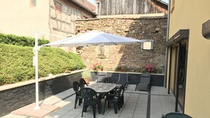An outdoor patio with a table and chairs, a stone wall, and a wooden building in the background. - 2-person apartment (Soultzmatt)