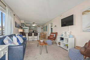 A living room with a sofa, a chair, a coffee table, a bookshelf, and a TV. - Beachside Condo - Sleeps 7! (Myrtle Beach)