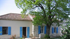 A two-story building with blue shutters, a tiled roof, and a garden area with small plants and a tree. - Beautiful old cottage, with a  rear terrace giving stunning panoramic views.  (Lacépède)
