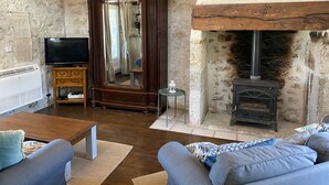A rustic living room with a stone wall, a wooden cabinet, a television, a sofa, and a fireplace. - Beautiful old cottage, with a  rear terrace giving stunning panoramic views.  (Lacépède)