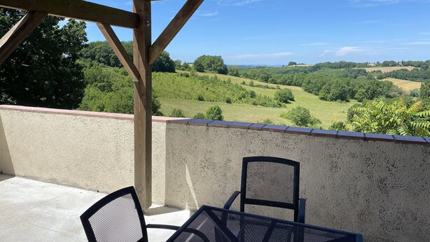 A covered outdoor area with a table and two chairs, overlooking a green landscape with trees and fields. - Beautiful old cottage, with a  rear terrace giving stunning panoramic views.  (Lacépède)