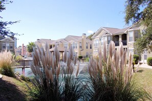 A residential area with multiple two-story houses, a small bridge over a water feature, and well-maintained landscaping including tall grasses.