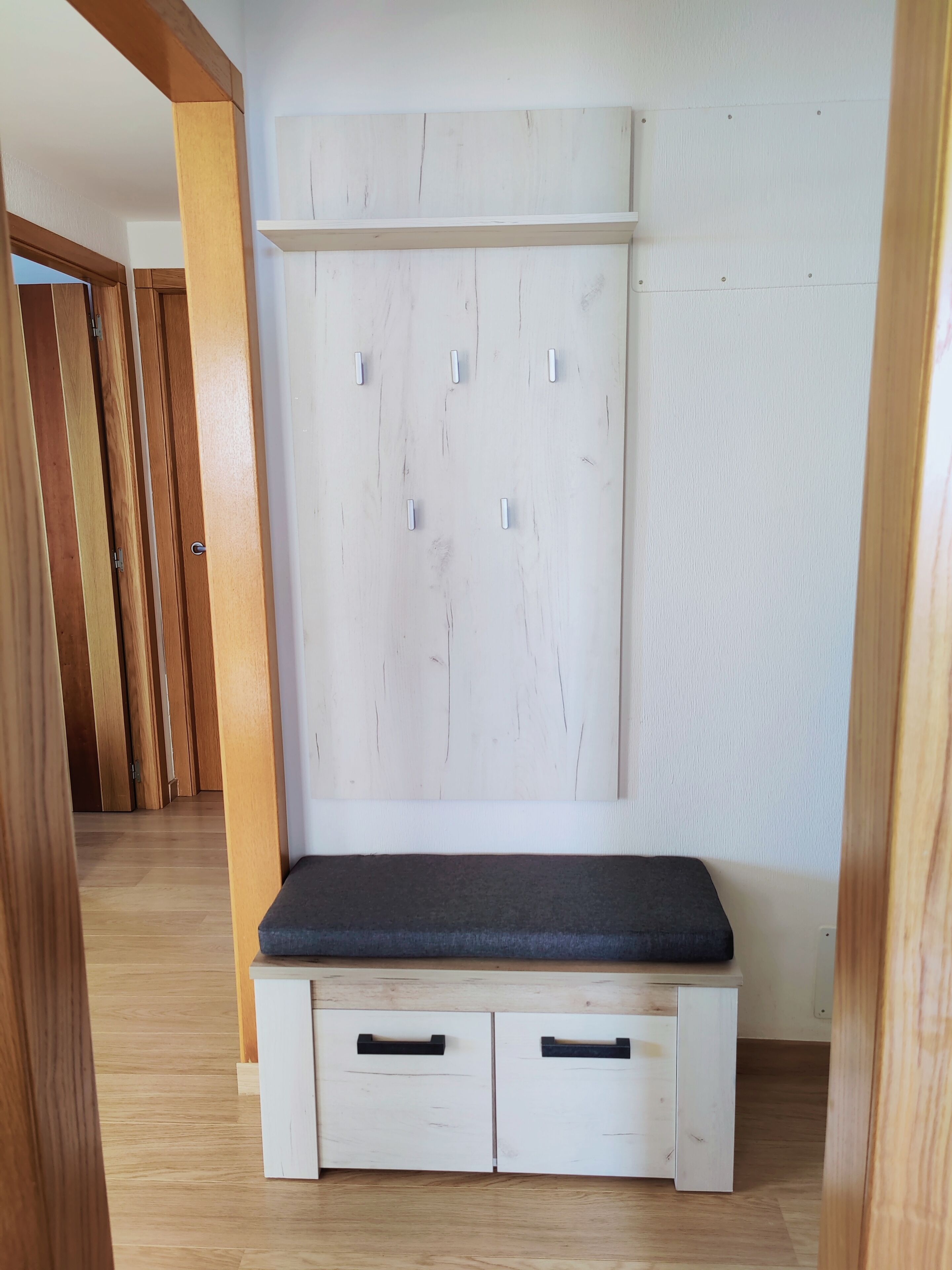 A room with a built-in bench, two drawers, and a white wall with a wooden panel.