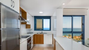 Eine moderne Küche mit Meerblick, ausgestattet mit einem Edelstahlkühlschrank, Holzschränken und einem großen Fenster.