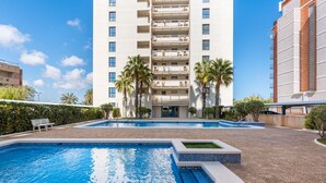 Ein Hotel mit Schwimmbad, Palmen und einem mehrstöckigen Gebäude mit Balkonen.