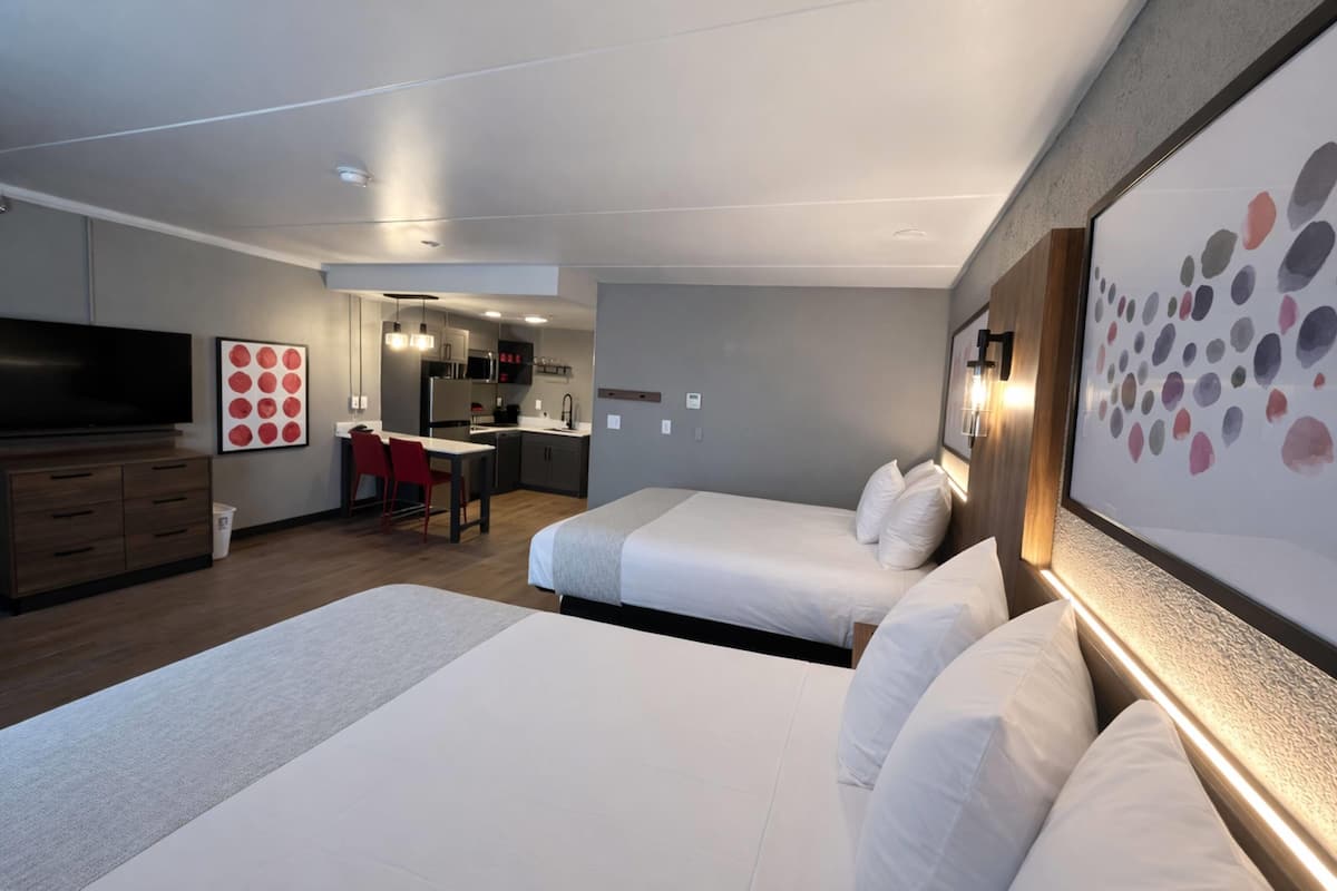Ein Hotelzimmer mit zwei Betten, einem Fernseher, einem Schreibtisch und einer Küchenzeile.