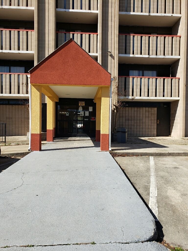 A building with a covered entrance, multiple balconies, and a parking area.