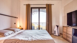 Habitación de hotel con cama, televisión, calefacción y balcón con cortinas.