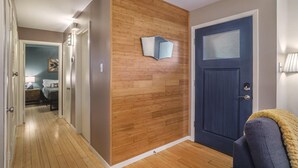 Ein Flur mit Holzboden, einer blauen Tür und einem Bett im Hintergrund.