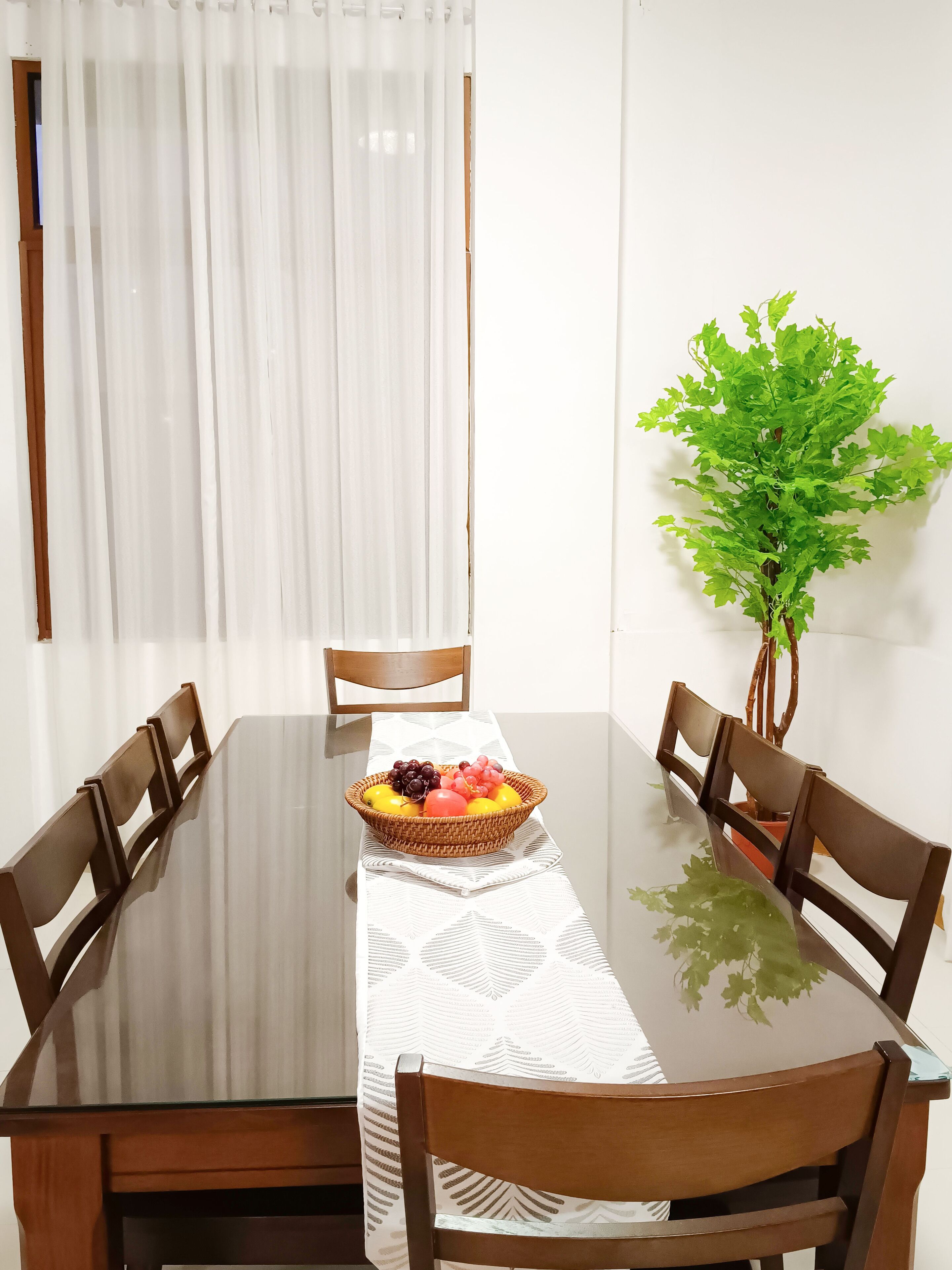 A dining table with a white tablecloth, surrounded by wooden chairs, and a fruit basket on the table.