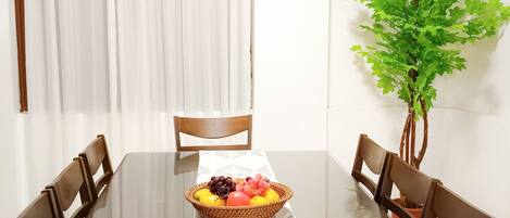 A dining table with a white tablecloth, surrounded by wooden chairs, and a fruit basket on the table.