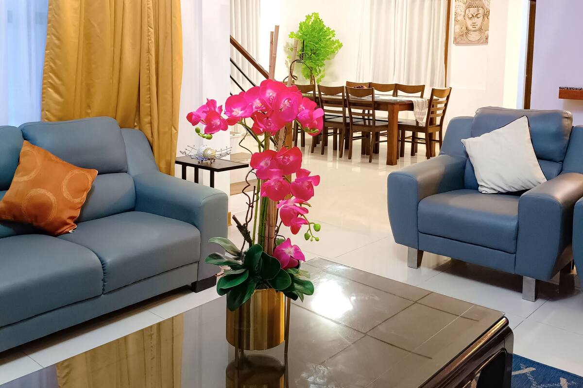 A modern hotel room with a sofa, armchair, and a coffee table with a vase of pink orchids.